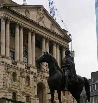 The Duke of Wellington statue on a tall stone pedestal, with a classical building and columns behind it.