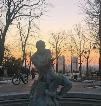 Fisherman Fountain statue wrestling with a large snake in a park at sunset.