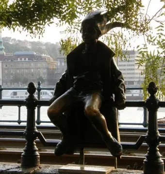 Little Princess bronze statue of a child in a cloak and jester cap beside a riverside railing.