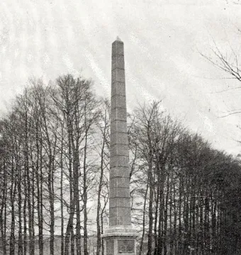 The Needle, a tall stone monument on a tiered base in a grassy clearing with bare trees behind it.