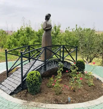 Bronze statue of Zabel Yessayan holding a book on a small arched bridge in a circular garden bed.