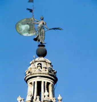 The Giraldillo statue holding a shield and palm branch atop the Giralda tower against a blue sky.