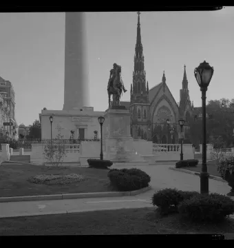 The Lafayette Monument with an equestrian statue on a stone pedestal, a tall column behind it, and a Gothic-style church nearby.