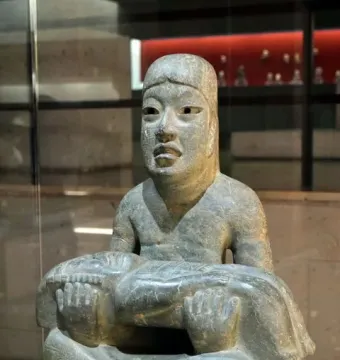 Las Limas Figurine showing a seated grey-green stone figure holding a smaller figure across its lap.
