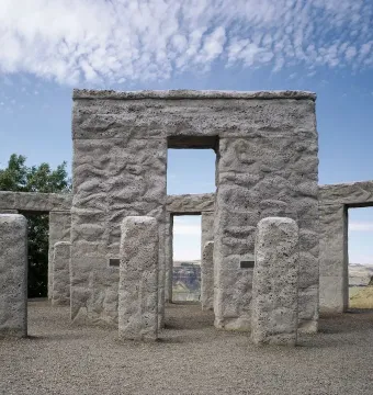 Maryhill Stonehenge with rough gray stone pillars and lintels framing a view of dry rolling hills under a blue sky.