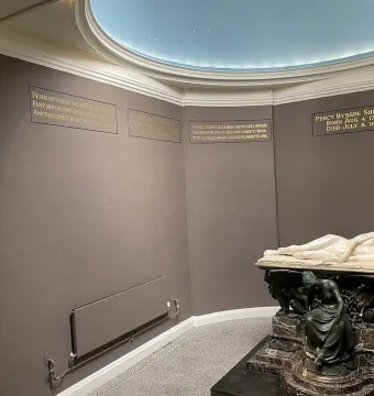 Shelley Memorial with a white marble reclining male figure on a sarcophagus, supported by a seated bronze figure.