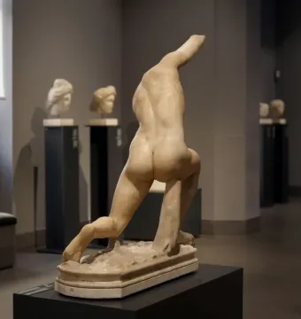 Back view of the Subiaco Ephebe sculpture on a pedestal in a museum gallery, missing its head and arms.