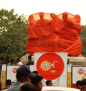 Anti Terrorism Raju Memorial Sculpture covered in bright orange fabric, with human-like figures visible at the top and a crowd in front.