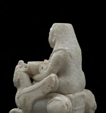 Lady of Galera carved stone figurine shown from the back and side, with an elaborate coiffure and a vessel in hand.
