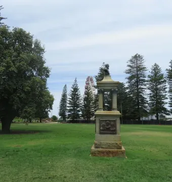 Maitland Brown Memorial stone monument with a bust and relief figures, with a Ferris wheel in the background.
