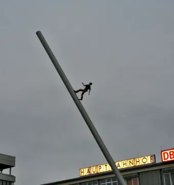 Man Walking to the Sky sculpture beside a slanted pole with the Hauptbahnhof building in the background.