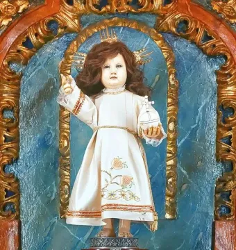 Santo Niño de Cebú statue in an ornate blue and gold shrine, dressed in a cream gown and holding a cross-topped orb.