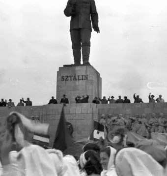 Stalin Monument with a towering statue on a stepped stone pedestal, with crowds gathered below and around the base.