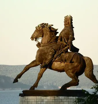 Tatishchev Monument showing a man in period clothing riding a rearing horse beside a wide river.