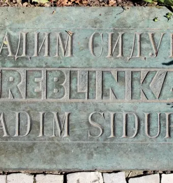 Weathered bronze Treblinka memorial plaque with carved Cyrillic and Latin text set into the ground.