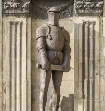 Wehrmann in Eisen, a dark armored knight statue with a hammer, standing on a carved pedestal against a stone facade.