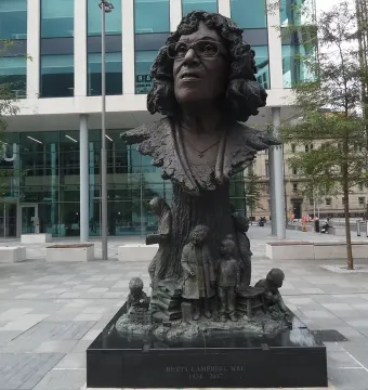Betty Campbell statue with a smiling bronze bust above figures of children on a tree trunk base.