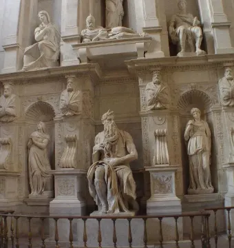 Marble statue of Moses seated with tablets under one arm, his other hand near his chin, with a long beard and horn-like protrusions on his head.