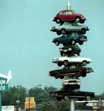 The Spindle sculpture with eight cars stacked vertically on a central pole above a shopping center sign.