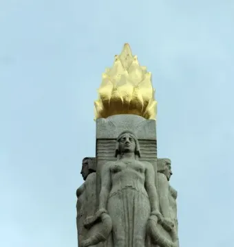 Upper section of the Titanic Engine Room Heroes Memorial with a gilded flame finial above carved female figures.