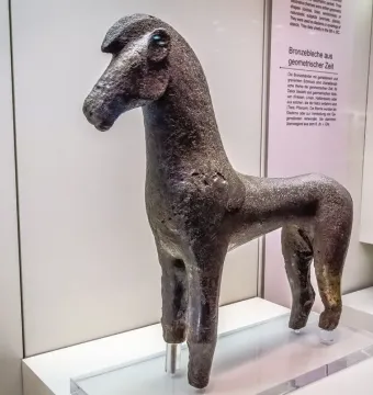 Dark bronze horse figurine with an elongated neck, prominent ears, and a textured surface on a clear display base.