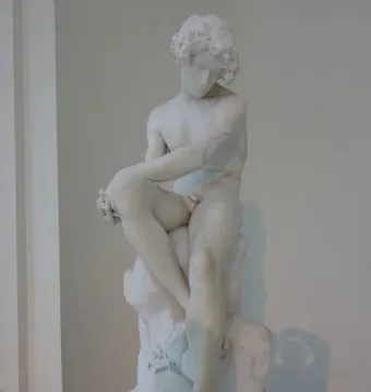 The Exiled, a white marble sculpture of a seated nude male figure with curly hair and a downcast expression.