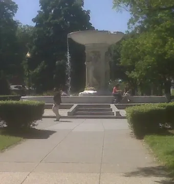 Dupont Circle Fountain in a green park with water flowing from the upper basin and people nearby.
