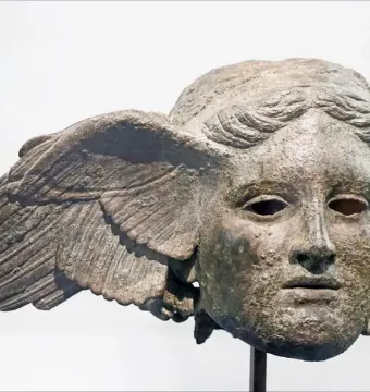 Bronze head of Hypnos with a green patina, serene face, and a wing extending from one side.