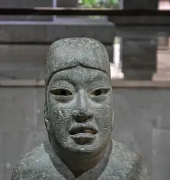 Las Limas Figurine showing a carved stone human figure with glyphs across the face, chest, and arm, holding a smaller figure.