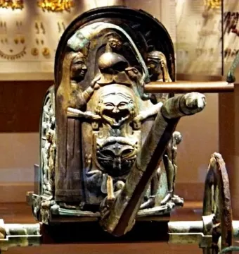 Front portion of the Monteleone Chariot with an ornate sculpted panel, mask-like faces, and a visible shaft extending forward.