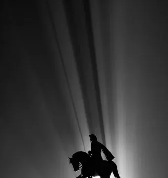 Silhouetted Sam Houston equestrian statue on a tall stone plinth with light beams radiating behind it.
