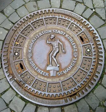 Koblenzer Schängel relief on a circular manhole cover in cobblestone pavement