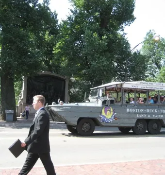 The Shaw Memorial appears behind trees and a stone wall, with a Boston Duck Tours vehicle passing in front.
