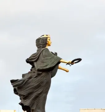 Statue of Sofia, a monumental female figure with a gilded face and crown, holding a wreath on a tall pedestal.