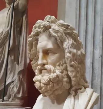 Marble bust of Zeus of Otricoli with a bearded face and curly hair, displayed on a pedestal in a museum gallery.