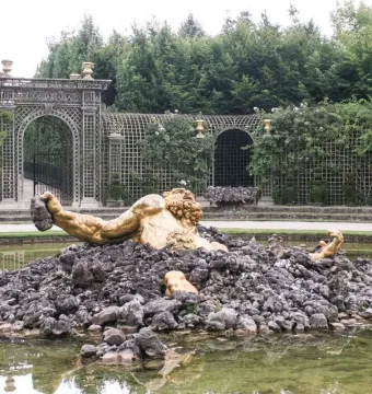 Enceladus Fountain showing a golden muscular figure rising from dark rocks in a greenish pool, with an arched trellis and greenery behind.