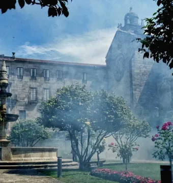 Herrería Fountain with water cascading into a circular stone basin, with trees and mist in the background.