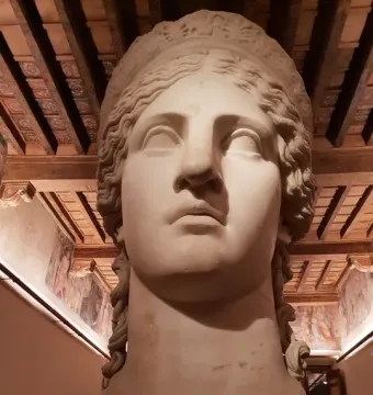 Juno Ludovisi marble head displayed in a room with ornate wooden ceiling and frescoed walls.