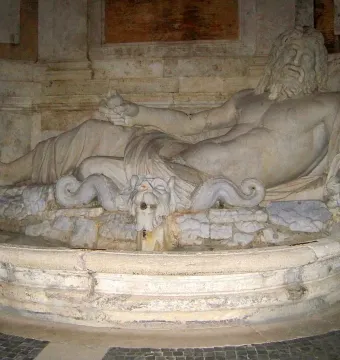 Marforio, a reclining stone male figure with water flowing from a beast-head spout into a basin.
