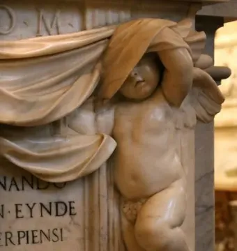Marble relief on the Tomb of Ferdinand van den Eynde showing a putto peeking from beneath draped cloth beside inscribed text.