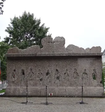 The Monument to Victims of the Wola Massacre, a rugged granite memorial with abstract human figures and circular recesses on its facade.