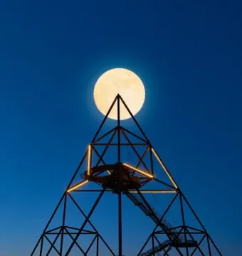 The Tetrahedron in Bottrop illuminated at twilight with a bright full moon above its apex.