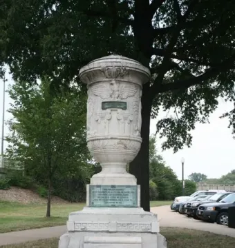 The Cuban Friendship Urn on a tiered stone pedestal with a bronze plaque, standing in a grassy park near a path and trees.