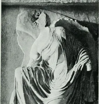Relief sculpture of Nike untieing her sandal, showing a draped female figure bent forward with her head partly obscured.
