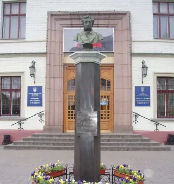 Weathered bronze Pushkin bust on a tall dark stone pedestal with flower boxes at the base