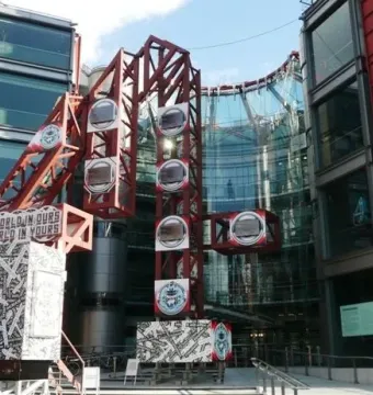 The Big 4 red metallic sculpture stands in front of a modern glass building, with patterned panels and the slogan \