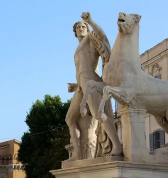 White marble Horse Tamers sculpture with a muscular figure beside a rearing horse on a stone pedestal.