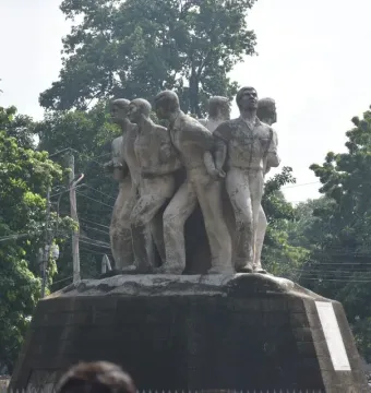 Anti Terrorism Raju Memorial Sculpture with several male figures in forward-moving poses on a dark pedestal, framed by trees.