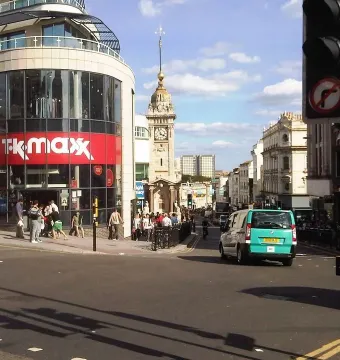 Brighton Clock Tower seen from street level between nearby buildings, with a pedestrian in the foreground and traffic lights on the right.