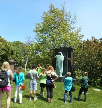 The Eternal Silence sculpture, a tall patinated bronze robed figure on a dark monument in a grassy setting with visitors nearby.